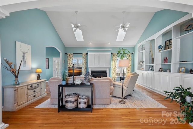 living room featuring light wood-type flooring, ceiling fan, a skylight, and built in features