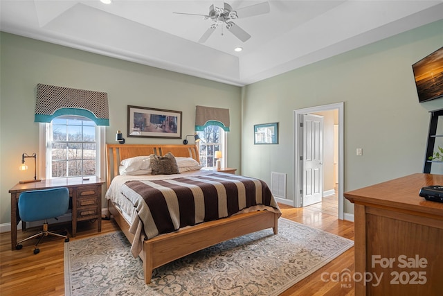 bedroom featuring ceiling fan, light wood-type flooring, and a tray ceiling