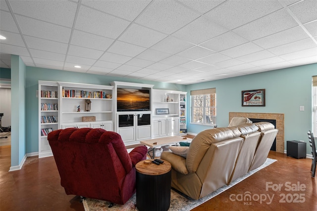 living room featuring a tiled fireplace, a drop ceiling, and built in shelves