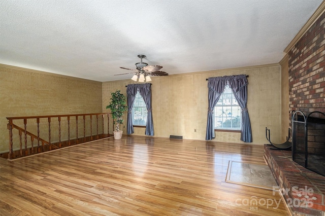 unfurnished living room featuring ceiling fan, hardwood / wood-style floors, a textured ceiling, and a brick fireplace