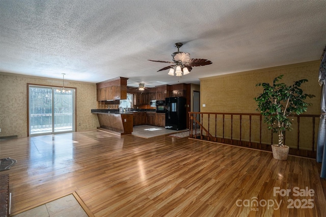 unfurnished living room with ceiling fan with notable chandelier, wood-type flooring, ornamental molding, and a textured ceiling