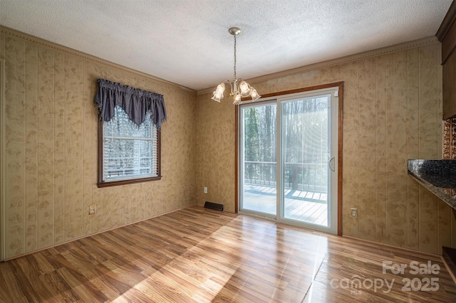 unfurnished dining area featuring light hardwood / wood-style floors, a textured ceiling, ornamental molding, and a notable chandelier