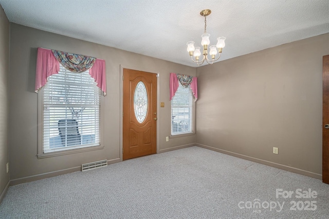 carpeted foyer entrance featuring an inviting chandelier, plenty of natural light, and a textured ceiling