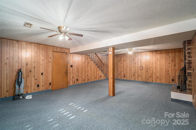 basement featuring a textured ceiling, wooden walls, and dark carpet