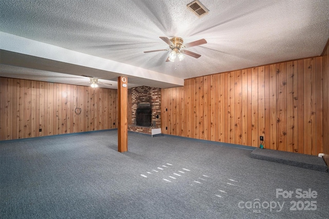 basement featuring wood walls, a textured ceiling, a fireplace, and carpet floors