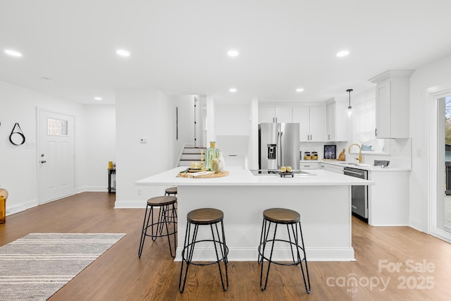 kitchen with appliances with stainless steel finishes, white cabinetry, sink, a center island, and light hardwood / wood-style flooring