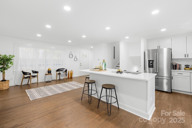 kitchen with dark wood-type flooring, high end refrigerator, white cabinets, and a center island with sink