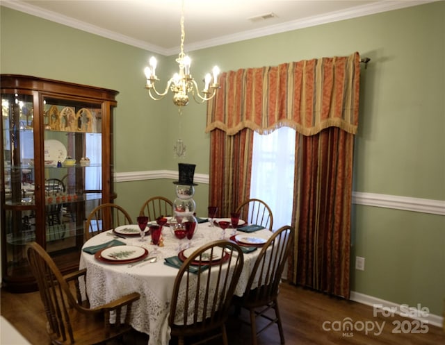 dining area featuring dark wood-type flooring, ornamental molding, and a notable chandelier