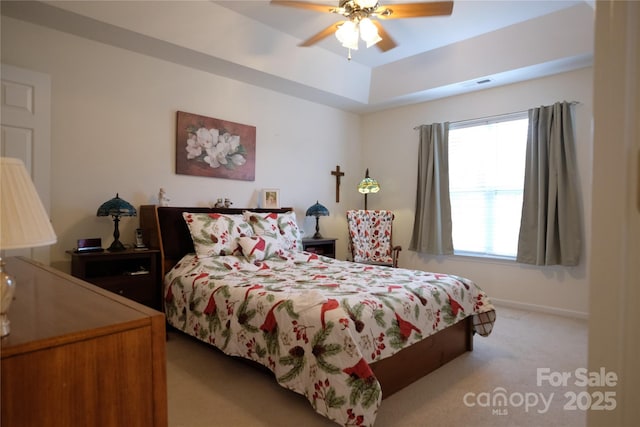 bedroom featuring light carpet, ceiling fan, and a tray ceiling