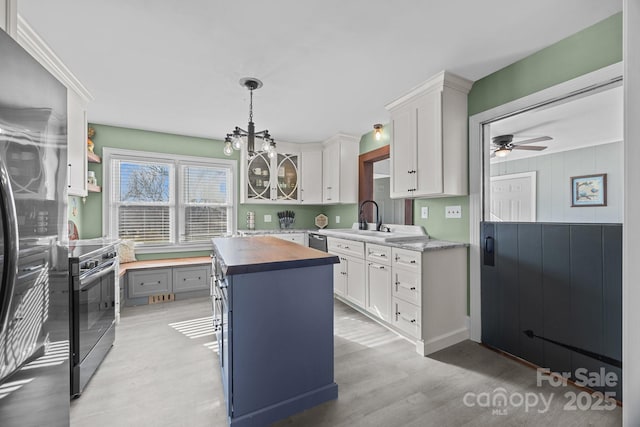 kitchen featuring hanging light fixtures, appliances with stainless steel finishes, white cabinetry, butcher block countertops, and a center island