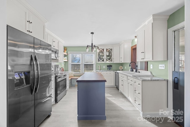 kitchen with butcher block counters, appliances with stainless steel finishes, white cabinetry, sink, and a kitchen island