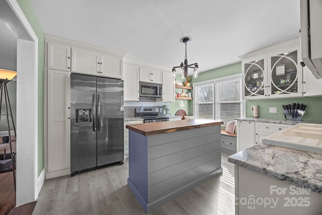 kitchen with white cabinets, wood counters, decorative light fixtures, stainless steel appliances, and light hardwood / wood-style floors