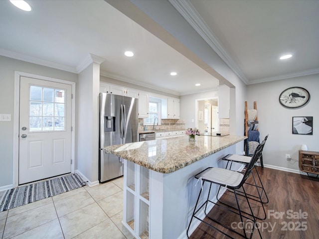 kitchen featuring decorative backsplash, light stone countertops, stainless steel appliances, ornamental molding, and white cabinets