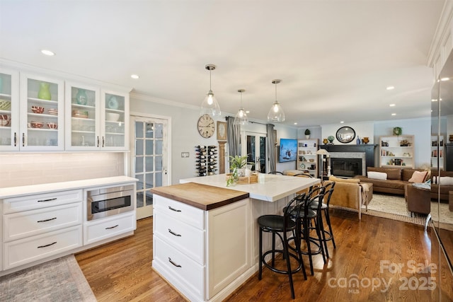 kitchen with white cabinets, a center island, backsplash, a brick fireplace, and stainless steel microwave