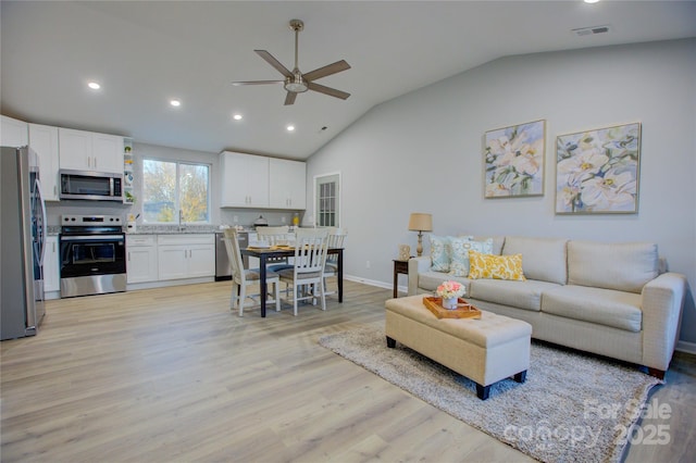 living room with ceiling fan, vaulted ceiling, and light hardwood / wood-style floors