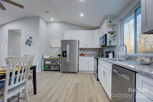 kitchen with light stone countertops, appliances with stainless steel finishes, lofted ceiling, white cabinetry, and sink