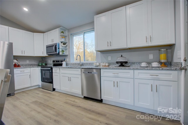 kitchen with light wood-type flooring, appliances with stainless steel finishes, white cabinetry, and light stone counters