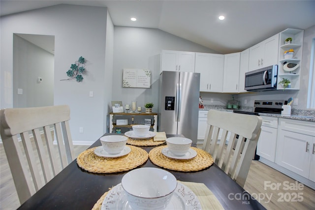 kitchen with light stone counters, white cabinets, appliances with stainless steel finishes, and lofted ceiling