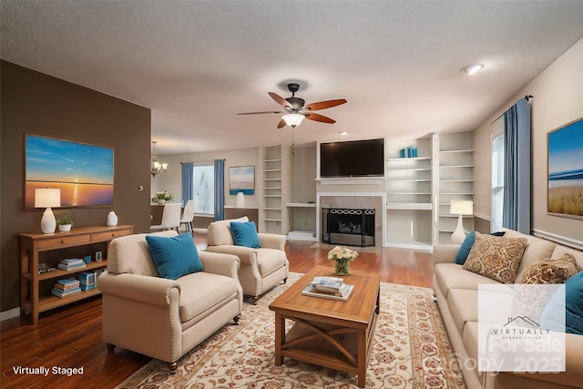 living room featuring a fireplace, ceiling fan with notable chandelier, built in shelves, and wood-type flooring