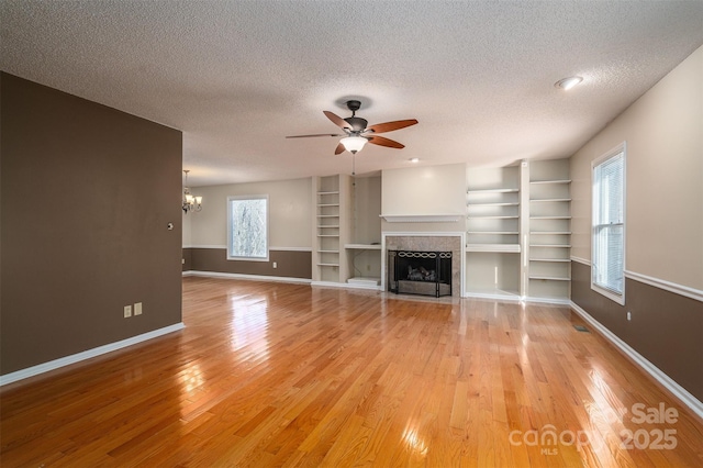 unfurnished living room with built in shelves, a tiled fireplace, a textured ceiling, and light wood-type flooring