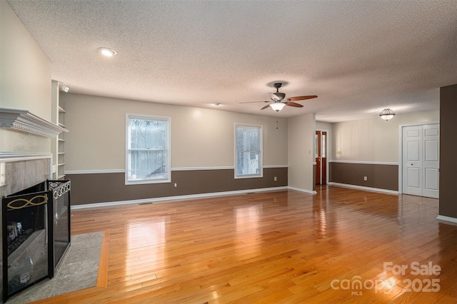 living room with ceiling fan, a fireplace, light hardwood / wood-style flooring, and a textured ceiling