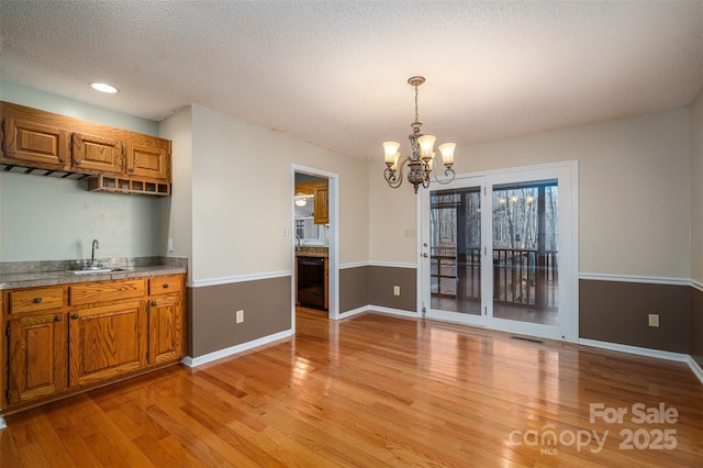 kitchen featuring sink, light hardwood / wood-style flooring, dishwasher, a textured ceiling, and decorative light fixtures