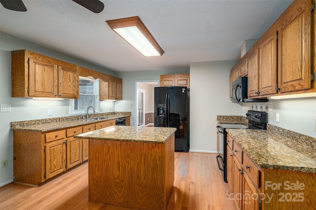 kitchen with light hardwood / wood-style flooring, stone countertops, black appliances, a kitchen island, and sink