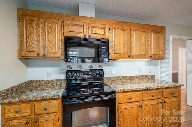 kitchen featuring light wood-type flooring, dark stone countertops, a textured ceiling, and black appliances