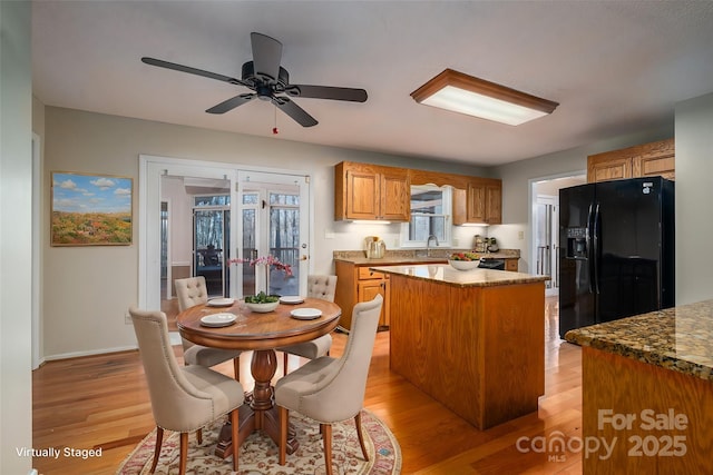 kitchen with ceiling fan, a center island, light hardwood / wood-style floors, and black fridge