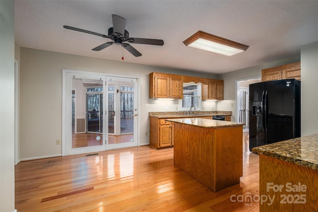 kitchen with black fridge with ice dispenser, a textured ceiling, light hardwood / wood-style flooring, a kitchen island, and dark stone counters