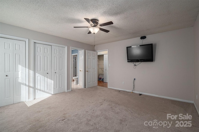 unfurnished bedroom featuring multiple closets, ensuite bath, ceiling fan, and carpet