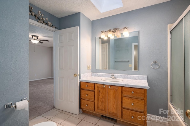 bathroom with a textured ceiling, a skylight, ceiling fan, tile patterned floors, and vanity