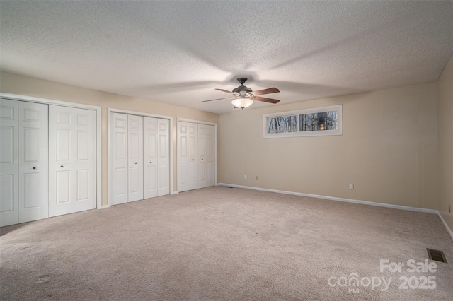 unfurnished bedroom with ceiling fan, carpet floors, a textured ceiling, and two closets