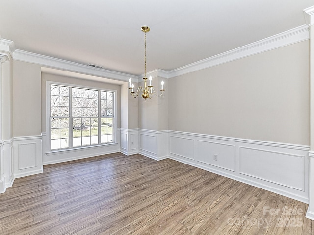 unfurnished dining area with hardwood / wood-style floors, ornamental molding, and an inviting chandelier