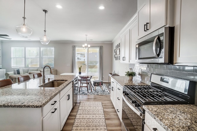 kitchen with a center island with sink, ornamental molding, a sink, wood finished floors, and appliances with stainless steel finishes