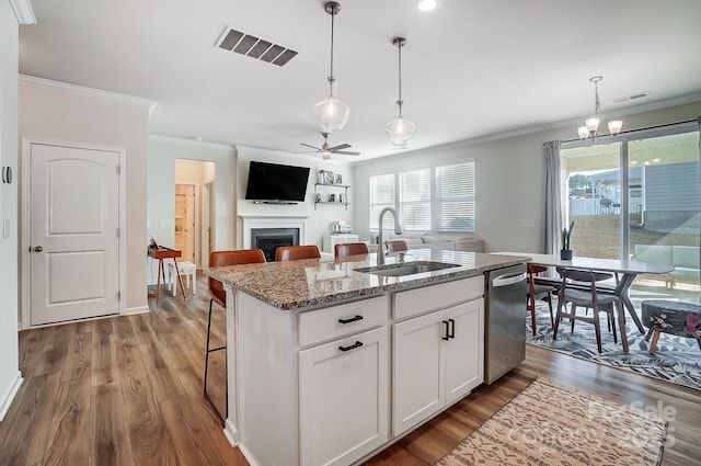 kitchen featuring white cabinetry, stainless steel dishwasher, an island with sink, pendant lighting, and light stone countertops