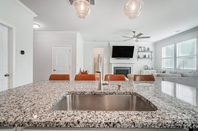 kitchen with a glass covered fireplace, crown molding, light stone countertops, and a sink