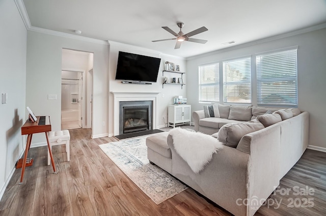 living area with visible vents, crown molding, ceiling fan, a fireplace with flush hearth, and wood finished floors