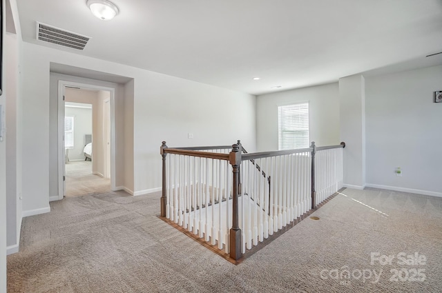 hallway with carpet flooring, an upstairs landing, visible vents, and baseboards