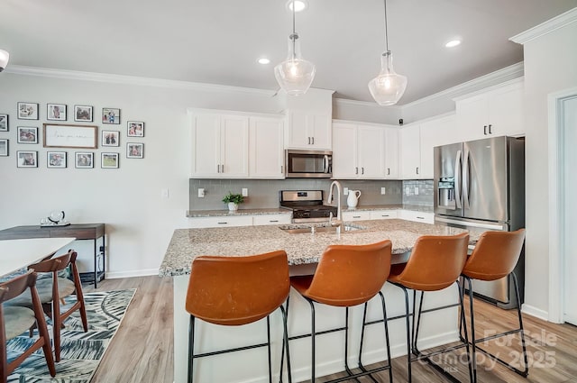 kitchen with light wood finished floors, ornamental molding, appliances with stainless steel finishes, white cabinetry, and a sink