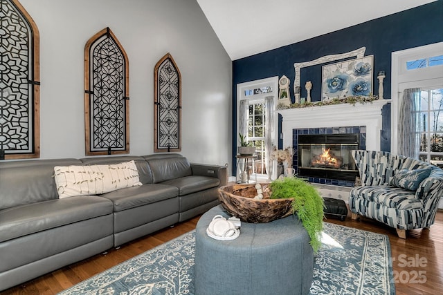 living room featuring lofted ceiling, a tiled fireplace, and wood-type flooring