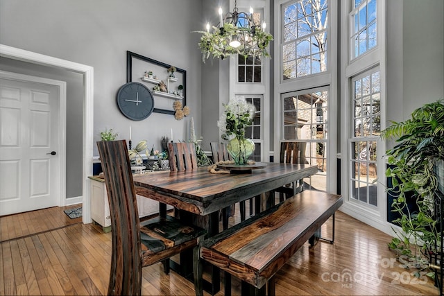 dining space with an inviting chandelier, a towering ceiling, and hardwood / wood-style floors