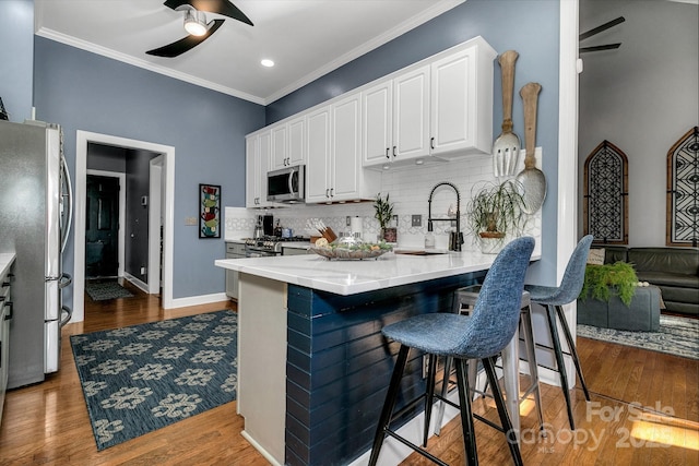 kitchen featuring hardwood / wood-style flooring, stainless steel appliances, a kitchen breakfast bar, and white cabinets