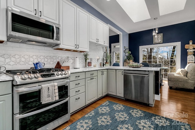 kitchen with white cabinets, dark hardwood / wood-style flooring, hanging light fixtures, kitchen peninsula, and stainless steel appliances