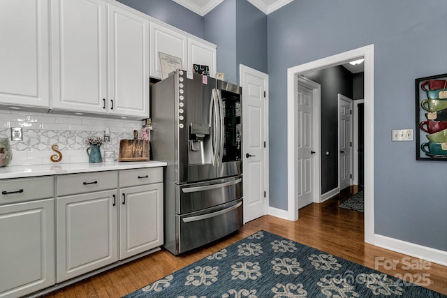 kitchen with dark wood-type flooring, stainless steel fridge, white cabinetry, backsplash, and ornamental molding