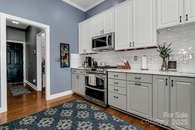 kitchen with crown molding, appliances with stainless steel finishes, dark hardwood / wood-style flooring, and white cabinets