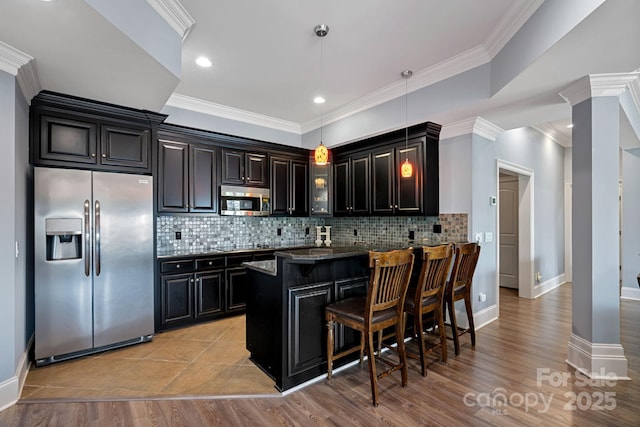 kitchen with decorative light fixtures, backsplash, a kitchen bar, ornamental molding, and stainless steel appliances