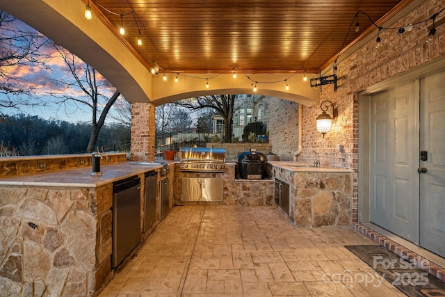 patio terrace at dusk featuring an outdoor kitchen, area for grilling, and sink