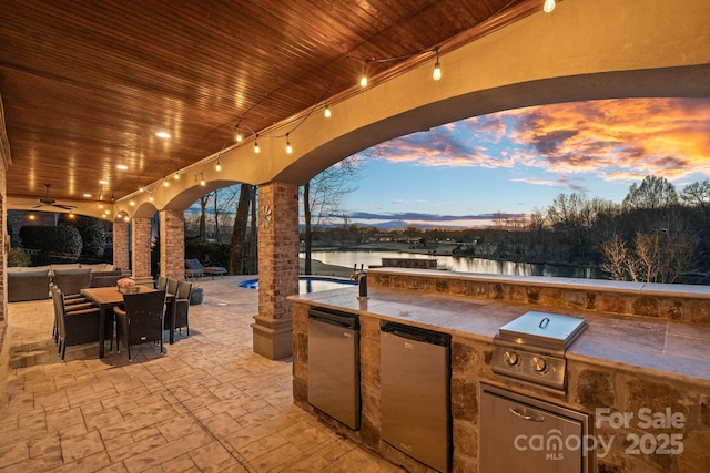 patio terrace at dusk featuring ceiling fan, a water view, area for grilling, and grilling area