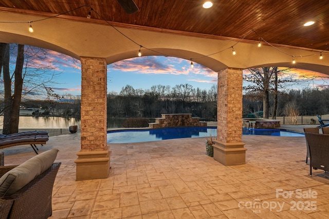 patio terrace at dusk with a water view, pool water feature, and a pool with hot tub